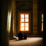 A father and child sit together in prayer inside a beautifully decorated mosque.
